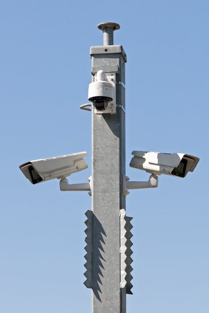 services-01 Outdoor surveillance system with multiple cameras mounted on a metal pole against blue sky.