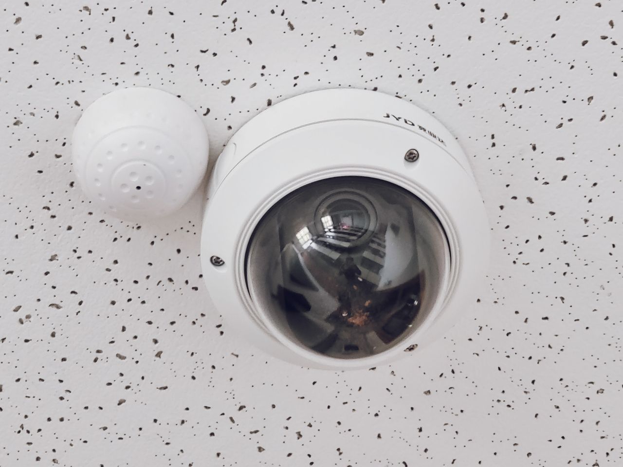 about-01 Close-up of a round dome surveillance camera installed on a speckled ceiling for security monitoring.